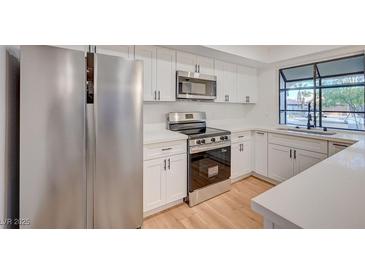 Modern kitchen featuring stainless steel appliances, white cabinetry, and a window overlooking the yard at 8412 Mulcahy Ave, Las Vegas, NV 89145