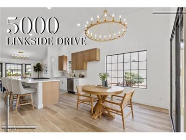 Bright kitchen features modern appliances, a light wood breakfast bar with seating, and dining table with statement chandelier at 5000 Linkside Dr, Las Vegas, NV 89130