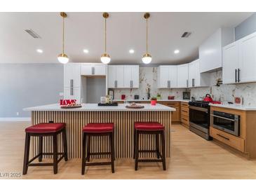 Modern kitchen with white cabinets, stainless steel appliances, marble backsplash, and a stylish island with seating at 6324 Eugene Ave, Las Vegas, NV 89108