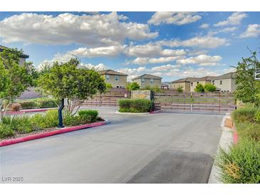 Community entrance with landscaped median, gate, and multi-story homes under a partly cloudy sky at 7052 Blissful Peak St, North Las Vegas, NV 89084
