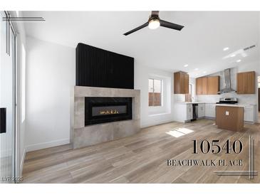 Open-concept living room with fireplace and wood-look tile flooring, and a peek into the kitchen at 10540 Beachwalk Pl, Las Vegas, NV 89144