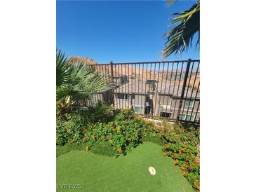 Green backyard with putting green, flowers, and views of the neighborhood beyond the metal fence at 44 Moon Hill Dr, Henderson, NV 89011