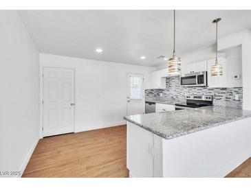 A beautifully renovated kitchen featuring white cabinets, stainless steel appliances, and granite countertops with modern hanging lights at 1121 W Monroe Ave, Las Vegas, NV 89106