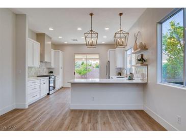 Bright kitchen features modern appliances, pendant lighting, white cabinets, and a counter with a bar overhang at 1506 Camino Summit Ave, Henderson, NV 89012