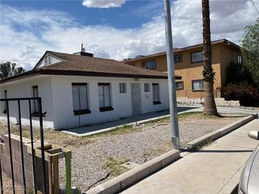 Cozy white home featuring a brown roof, complemented by a gravel front yard and a mature palm tree at 2417 St George St, North Las Vegas, NV 89030
