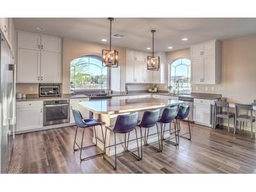 Bright open kitchen with hardwood flooring, large island with seating, modern lighting fixtures, and stainless steel appliances at 10047 Alden Creek St, Las Vegas, NV 89141