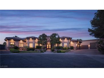 Stunning single-story home with stone accents, lush landscaping, and a circular driveway at twilight at 8620 W La Madre Way, Las Vegas, NV 89149