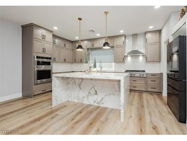 A modern kitchen featuring a marble waterfall island, stainless steel appliances, and light wood-colored cabinets at 8095 Carpenter Creek Ave, Las Vegas, NV 89113