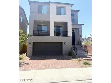 Two-story home featuring a balcony, two-car garage, and brick paved driveway at 7499 Lodano Ave, Las Vegas, NV 89113