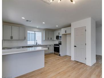 Bright, open kitchen featuring stainless steel appliances, light gray cabinets, and a spacious island with light wood floors at 9855 Ashton Pines Ct, Las Vegas, NV 89147
