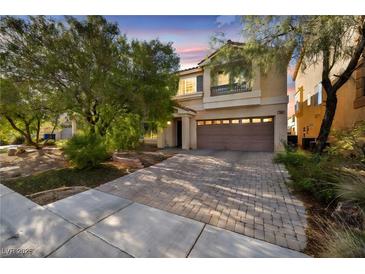 Two-story home with neutral paint, balcony, brick driveway and mature trees at dusk at 5080 Plymouth Bay Ct, Las Vegas, NV 89141