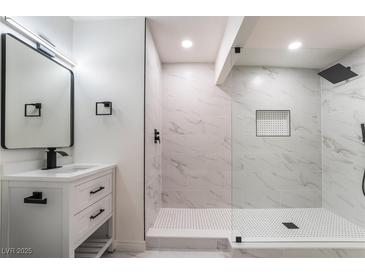 Modern bathroom featuring marble tile, glass shower, white vanity with black fixtures, and a contemporary mirror at 934 Lewis Ct, Henderson, NV 89015