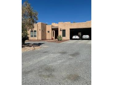 Beige house with desert landscaping and a two-car garage beneath the main structure at 3551 Sagebrush Ave, Pahrump, NV 89048