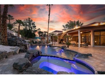 An amazing outdoor area with a custom rock waterfall, gorgeous pool and spa highlighted by a fiery sunset at 2101 Diamond Bar Dr, Las Vegas, NV 89117