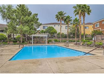 Relaxing community pool with lounge chairs and covered seating area surrounded by lush landscaping and palm trees at 9303 Gilcrease Ave # 1002, Las Vegas, NV 89149