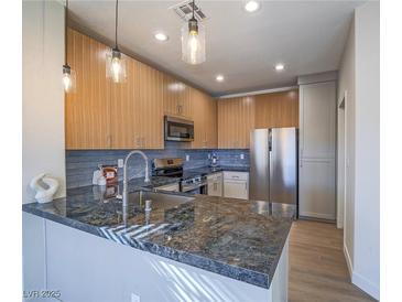 Modern kitchen with wood cabinetry, stainless steel appliances, and a beautiful dark stone breakfast bar at 1510 Fieldbrook St, Henderson, NV 89052