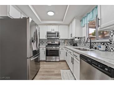 Updated kitchen boasts stainless steel appliances, white cabinets, black hardware, and patterned tile backsplash at 2507 Albemarle Way, Henderson, NV 89014