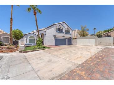 Two-story home featuring a two-car garage, a well-manicured lawn and palm trees on a sunny day at 4871 La Princesa Ct, North Las Vegas, NV 89031
