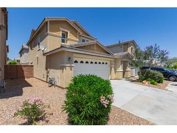 Two-story tan home with a two car garage, landscaping and a paved driveway at 104 Big Cliff Ave, North Las Vegas, NV 89031