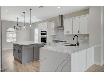 Bright open kitchen boasts white cabinets, stainless appliances, and an island with marble countertop and pendant lighting at 2603 Savannah Springs Ave, Henderson, NV 89052