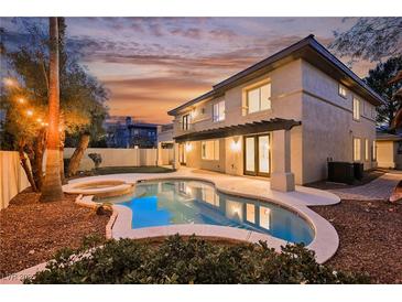 Beautiful backyard pool and spa with outdoor lighting, covered patio, and manicured landscaping at sunset at 516 Pinnacle Heights Ln, Las Vegas, NV 89144