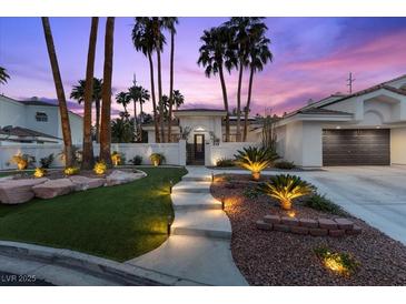 Beautiful home featuring manicured landscaping, an illuminated walkway, and mature palm trees in a desert setting at 219 Windsong Dr, Henderson, NV 89074