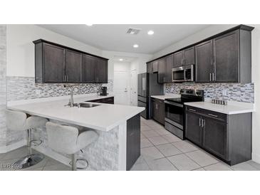 Modern kitchen features stainless steel appliances, mosaic backsplash, and quartz countertops with a breakfast bar at 5255 Peak Rock Ct, Las Vegas, NV 89141