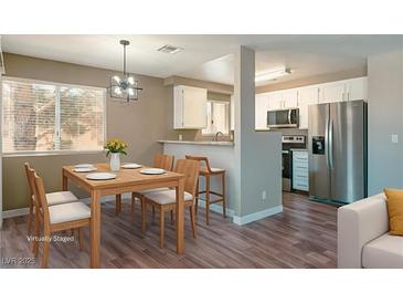 Bright dining area with wood table and modern lighting fixture adjacent to the kitchen featuring stainless steel appliances at 6873 Tamarus St # 201, Las Vegas, NV 89119