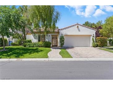 Charming single-story home with a manicured lawn, brick driveway, and lush, mature landscaping at 11775 Woodbrook Ct, Las Vegas, NV 89141