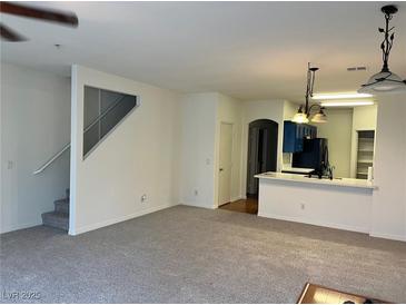 Spacious living room featuring neutral carpet, staircase, and access to the kitchen at 6462 Saddle Up Ave # 103, Henderson, NV 89011