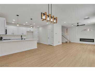 Open-concept living room with modern light fixtures, white kitchen, and sleek fireplace at 715 Taliput Palm Pl, Henderson, NV 89011