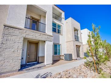 Charming townhome featuring a mix of stucco and stone facade, complemented by a black metal balcony and manicured landscaping at 6288 Dolosonte St, Las Vegas, NV 89113