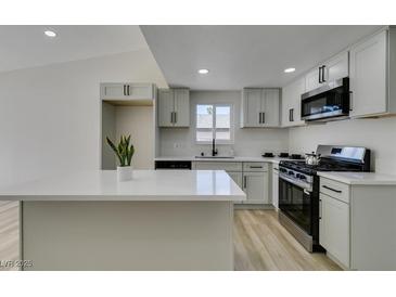 Modern kitchen boasts white cabinets, stainless steel appliances, and a center island with a white countertop at 706 Greenway Rd, Henderson, NV 89002