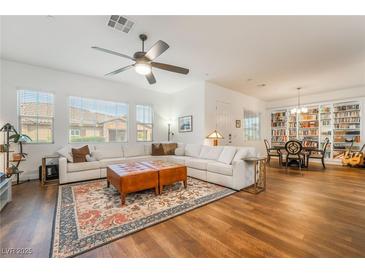 Bright living room featuring a large white sectional sofa, wood floors, ceiling fan, and an adjacent dining area at 715 Orange Plume Walk, Henderson, NV 89011