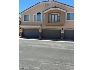 Exterior view of townhome with gray garage doors, second story balcony and neutral stucco finish at 3609 Indigo Flower St # 1, North Las Vegas, NV 89084