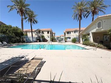 Community pool surrounded by palm trees and lounge chairs for relaxing, set between apartment buildings at 1881 W Alexander Rd # 2129, North Las Vegas, NV 89032
