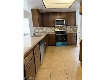 Kitchen featuring wooden cabinets, stainless steel appliances, and tile flooring at 5389 Spencer St, Las Vegas, NV 89119