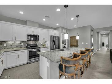 Modern kitchen with white cabinets, stainless steel appliances, granite counters and island with bar stool seating at 708 Kibbey St, Las Vegas, NV 89178