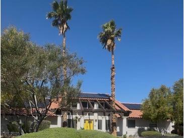 Charming desert home featuring solar panels, tile roof, and front yard palm trees at 1871 Ski Slope Cir, Las Vegas, NV 89117