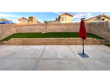 Well-kept backyard featuring a concrete patio, stone retaining wall, synthetic grass, and block fence at 2813 Painted Rose Ln, Henderson, NV 89074