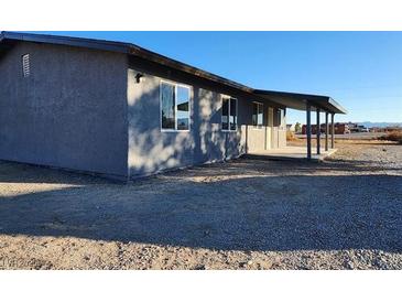 Side view of a home featuring a covered porch, gray siding, and gravel yard at 4231 E Kellogg Rd, Pahrump, NV 89061