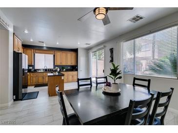 Open kitchen with wood cabinets and a black island adjacent to a formal dining area with black table at 11004 Napa Ridge Dr, Las Vegas, NV 89144