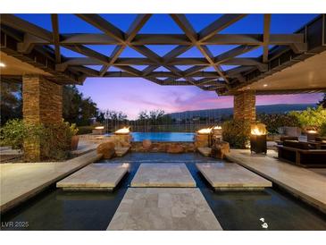 Stunning outdoor pool area featuring fire pits, stone accents, and a covered lounge space, perfect for evening relaxation at 11 Golden Sunray Ln, Las Vegas, NV 89135