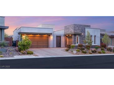 Modern home showcasing stone accents, a two-car garage, and well-manicured landscaping at sunset at 10482 Calico Terrace Ave, Las Vegas, NV 89135