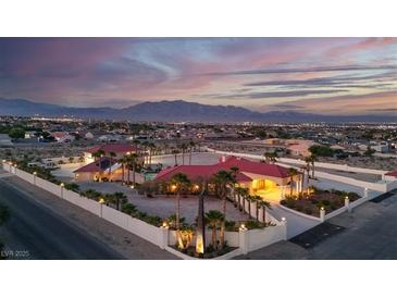 Expansive estate with red tile roof, palm trees, a pool, set against a stunning mountain backdrop at dusk at 10280 W La Mancha Ave, Las Vegas, NV 89149