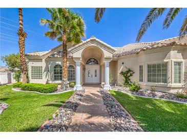 Inviting single-story home with lush landscaping, a stone walkway, and a charming arched entryway framed by palm trees at 2201 Country Cottage Ct, Las Vegas, NV 89117