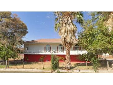 Charming two-story home with white balcony, red trim, and a desert landscape with mature trees in front at 2855 Rice St, Logandale, NV 89021