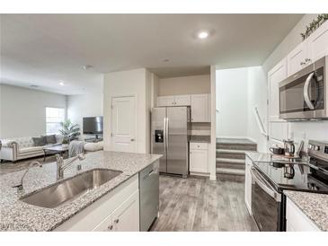 Modern kitchen features stainless steel appliances, gray countertop island, and open floor plan to the living room at 12728 Feathersong St, Henderson, NV 89044