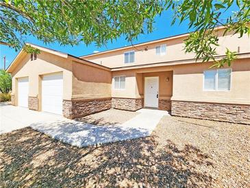 Charming townhome featuring a stone facade, a two-car garage, and mature trees for shade and curb appeal at 1951 Teepee Rd, Pahrump, NV 89048