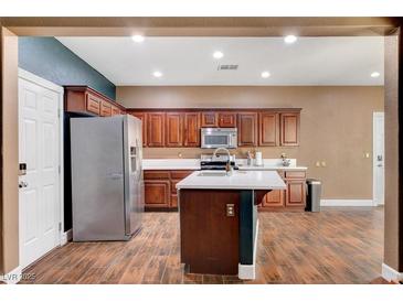 Well-lit kitchen features wood cabinetry, stainless steel appliances, an island, and wood-style floors at 8560 Alocasia Ct, Las Vegas, NV 89149